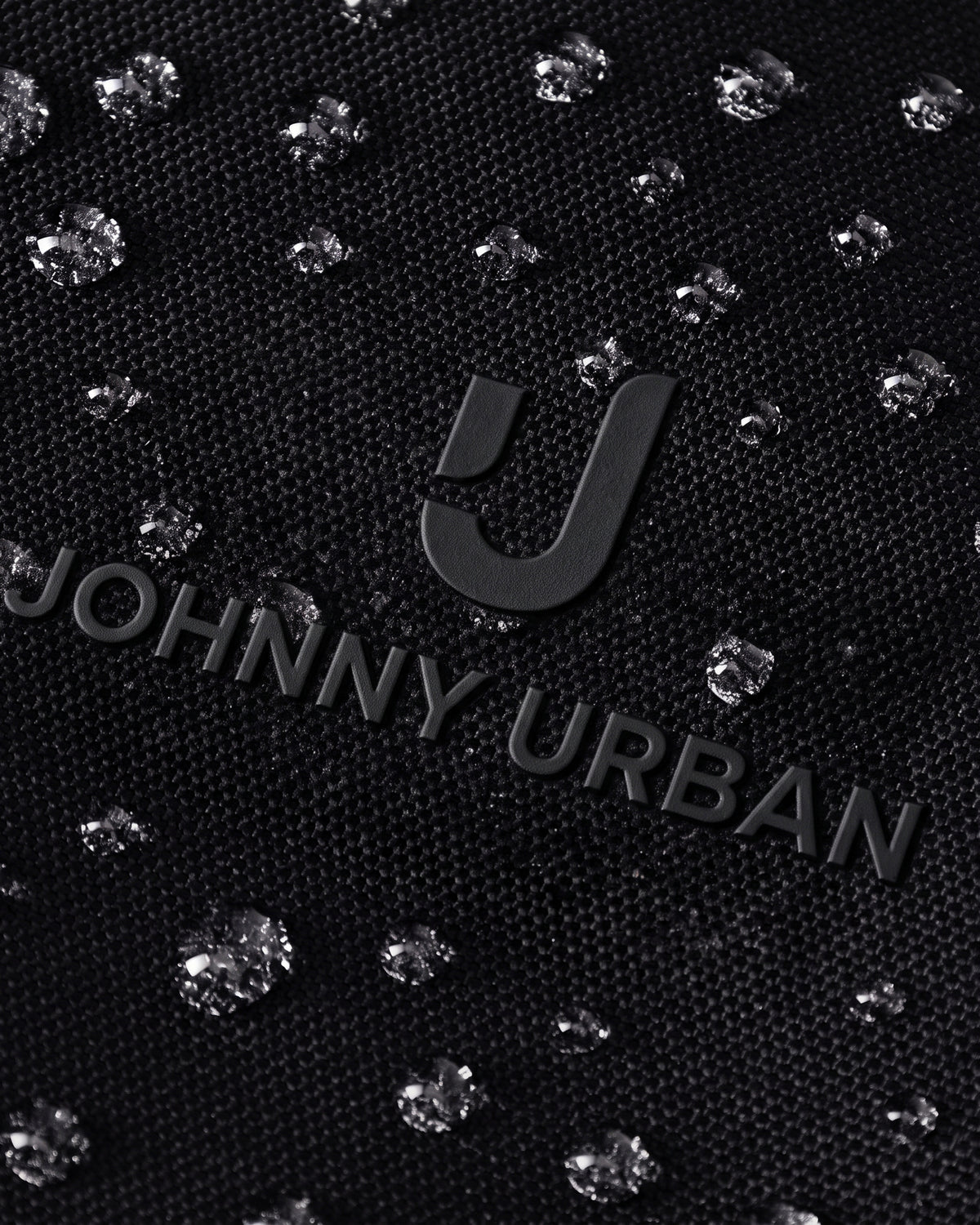 Nahe Aufnahme des schwarzen Johnny Urban Logos auf wasserabweisendem Stoff mit glänzenden Wassertropfen