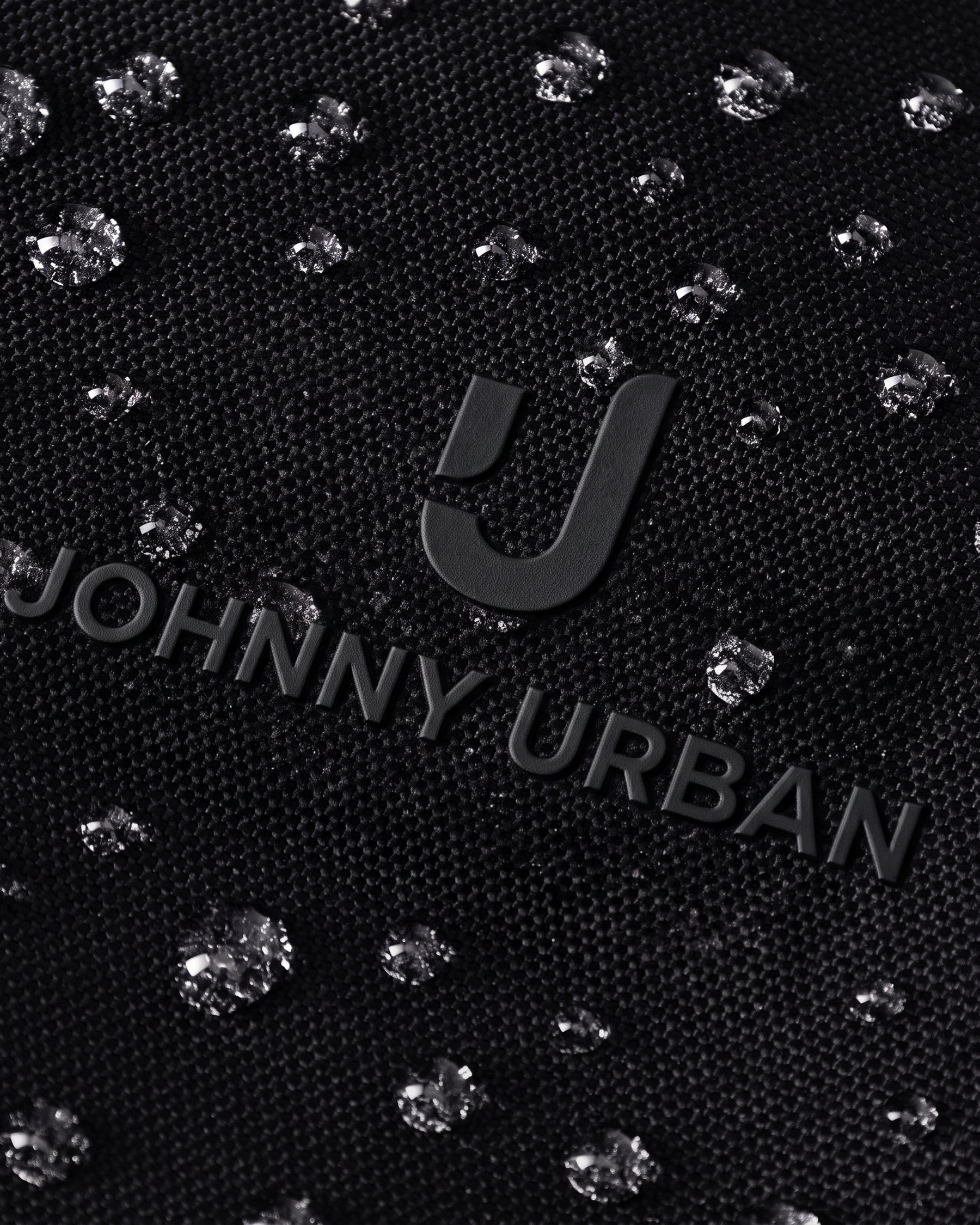 Nahe Aufnahme des schwarzen Johnny Urban Logos auf wasserabweisendem Stoff mit glänzenden Wassertropfen