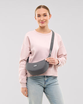 Frau mit dunkelgrauer Half Moon Bag 'Ally Small' von Johnny Urban, trägt rosa Pullover und Jeans