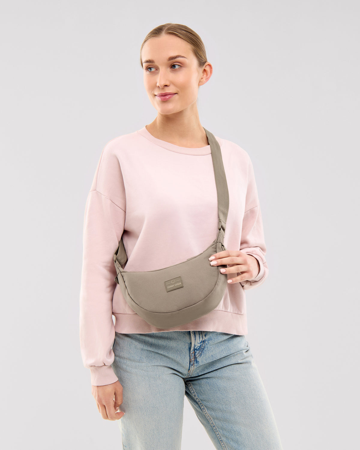 Frau trägt Half Moon Bag 'Ally Small' in desert grey, kombiniert mit hellem Pullover und Jeans