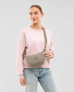 Frau trägt Half Moon Bag 'Ally Small' in desert grey, kombiniert mit hellem Pullover und Jeans
