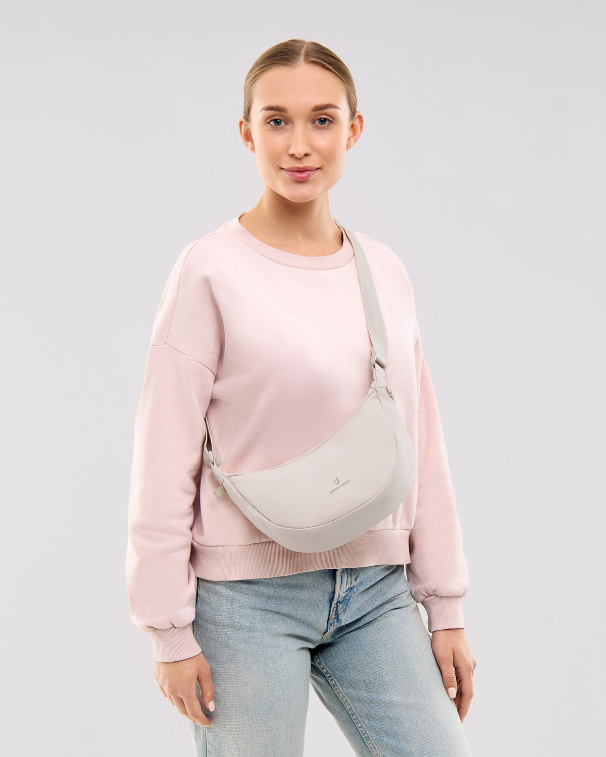 Frau trägt Half Moon Bag 'Ally Small' in Sandfarben, kombiniert mit hellem Pullover und Jeans