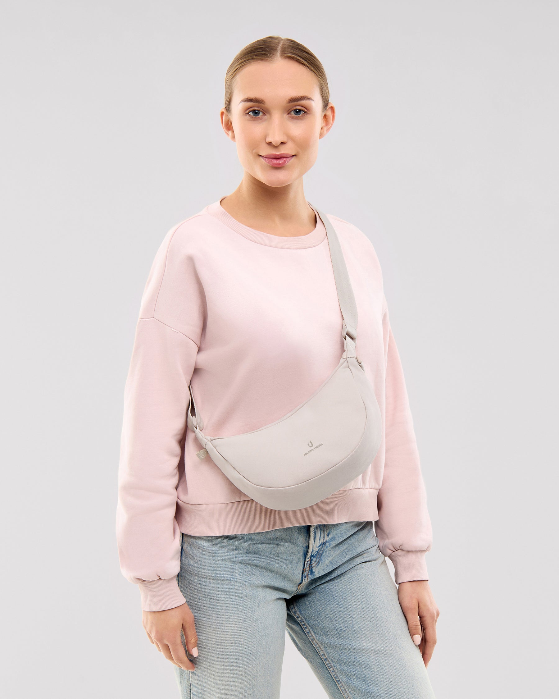 Frau trägt Half Moon Bag 'Ally Small' in Sandfarben, kombiniert mit hellem Pullover und Jeans
