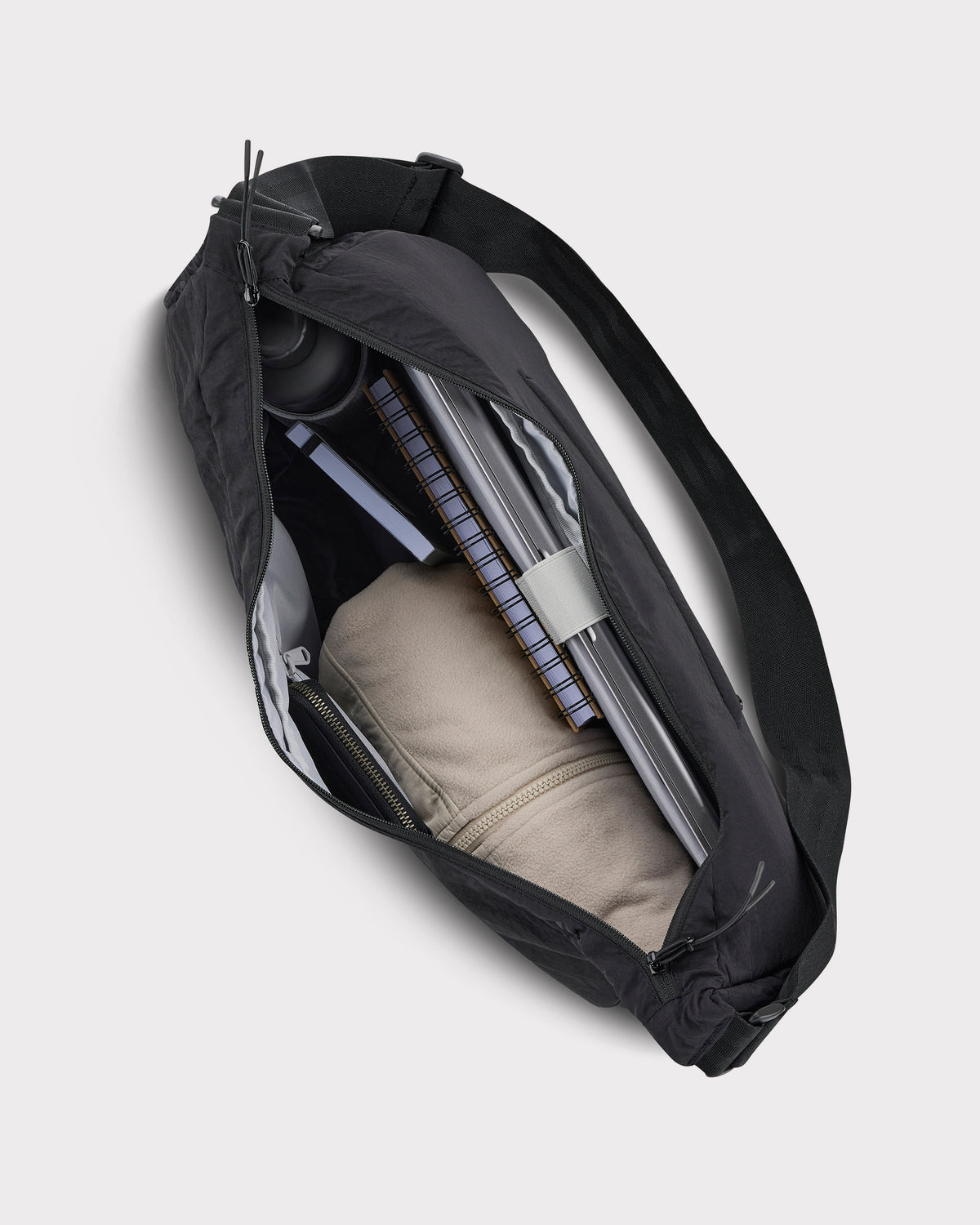 Schwarze Half Moon Bag 'Kaia XL' mit Reißverschluss, gefüllt mit Laptop, Notizbuch, Trinkflasche und beige Jacke