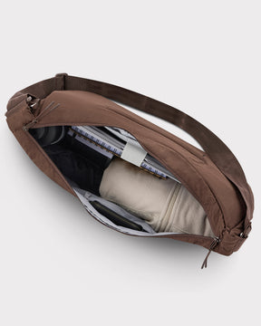 Halbmond-Tasche 'Kaia XL' in Dunkelbraun mit Reißverschluss geöffnet, zeigt Innenfächer mit Notizbuch, Kleidungsstück und Geldbörse
