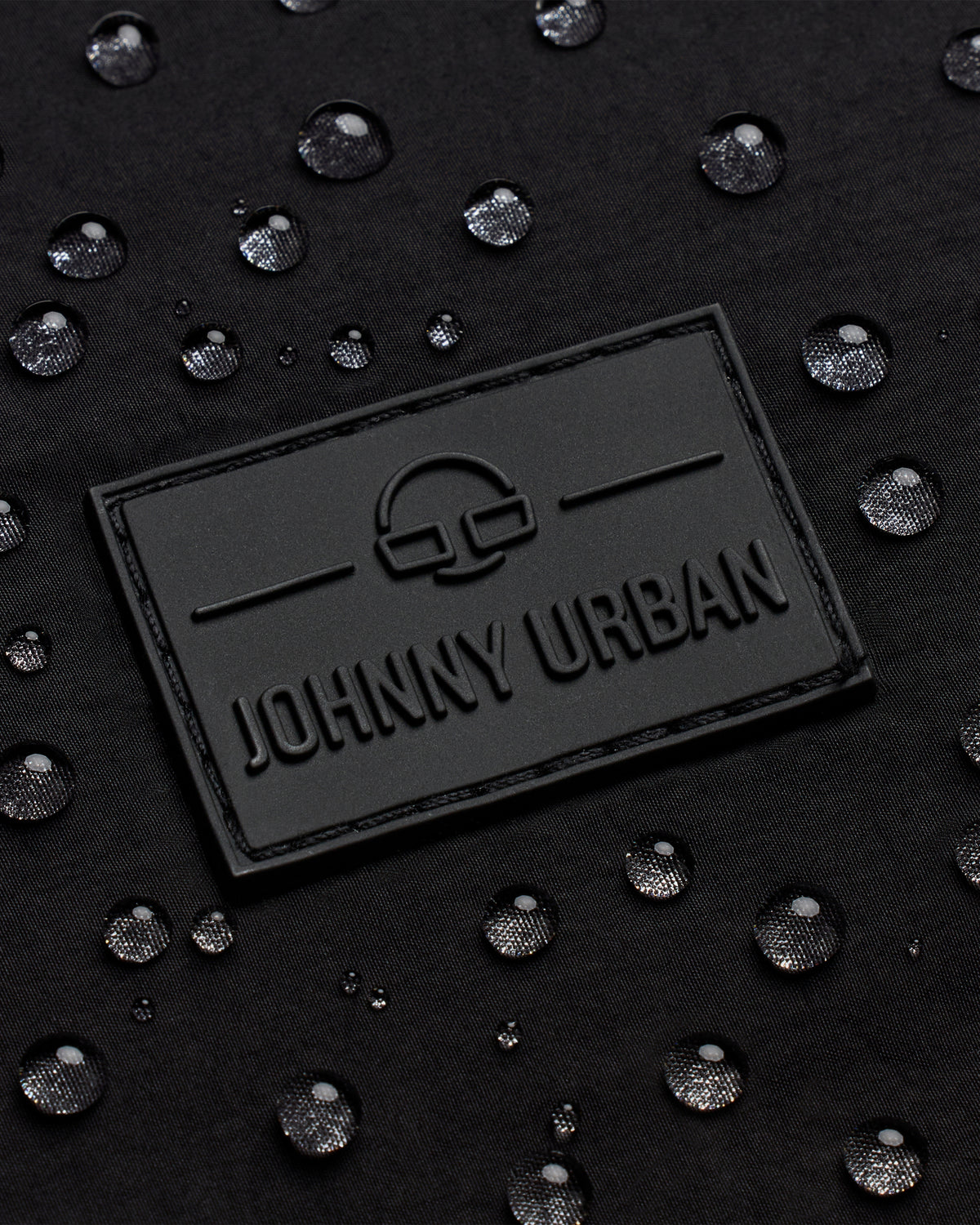 Schwarzes geprägtes Johnny Urban Logo auf wasserabweisendem Material mit Wassertropfen