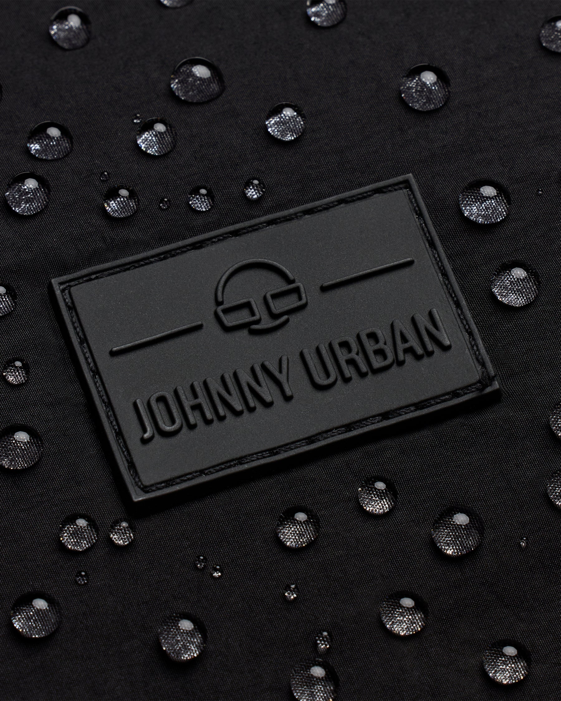 Schwarzes geprägtes Johnny Urban Logo auf wasserabweisendem Material mit Wassertropfen