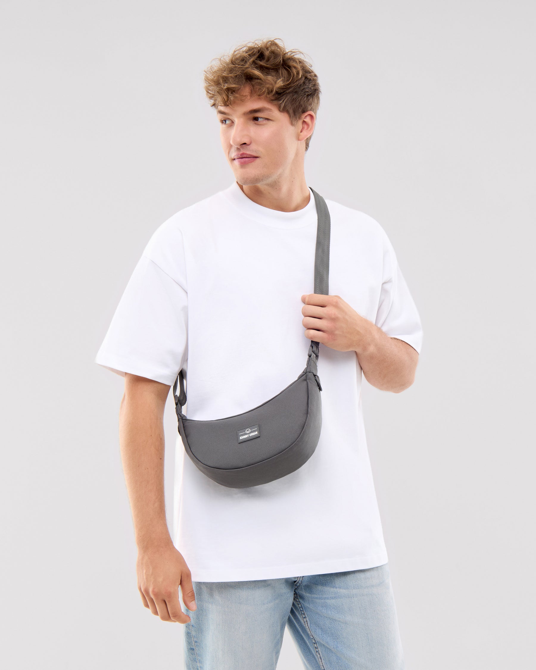 Mann trägt Half Moon Bag 'Ally Small' in dunklem Grau über der Schulter, kombiniert mit weißem T-Shirt und hellblauen Jeans