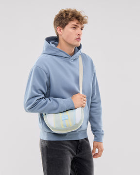Mann trägt kleine Half Moon Bag 'Ally Small' in Sand mit Streifen und hellblauen Hoodie