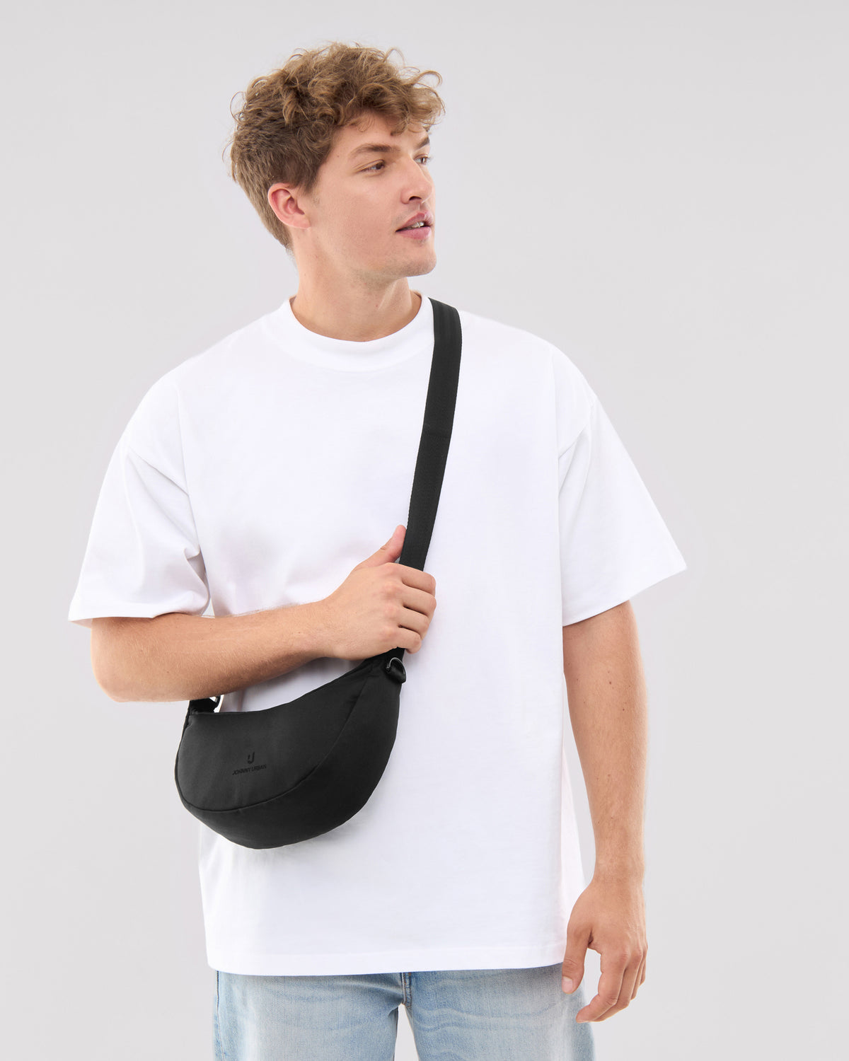 Mann trägt Johnny Urban Half Moon Bag 'Ally Small' in Schwarz quer über den Oberkörper