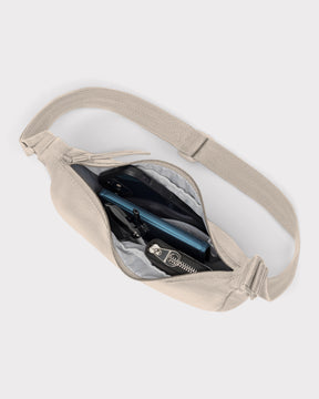 Sandfarbene Half Moon Bag 'Kaia Small' mit geöffnetem Reißverschluss und sichtbarem Smartphone, Schlüssel und Geldbörse innen