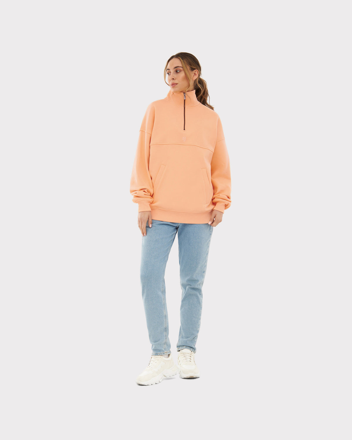Frau trägt Peach-farbenen Half Zip Sweatshirt 'Cooper' von Johnny Urban mit hellblauen Jeans und weißen Schuhen