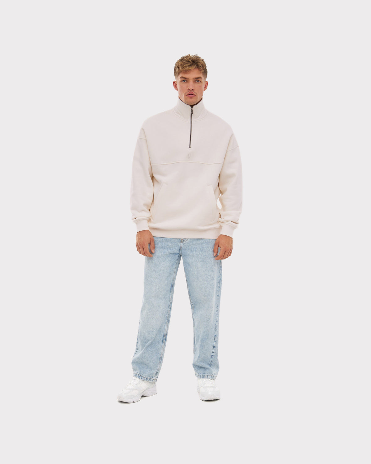 Herren trägt cremeweißen Half Zip Sweatshirt 'Cooper' mit Reißverschluss bis zur Brust und hellblaue Jeans