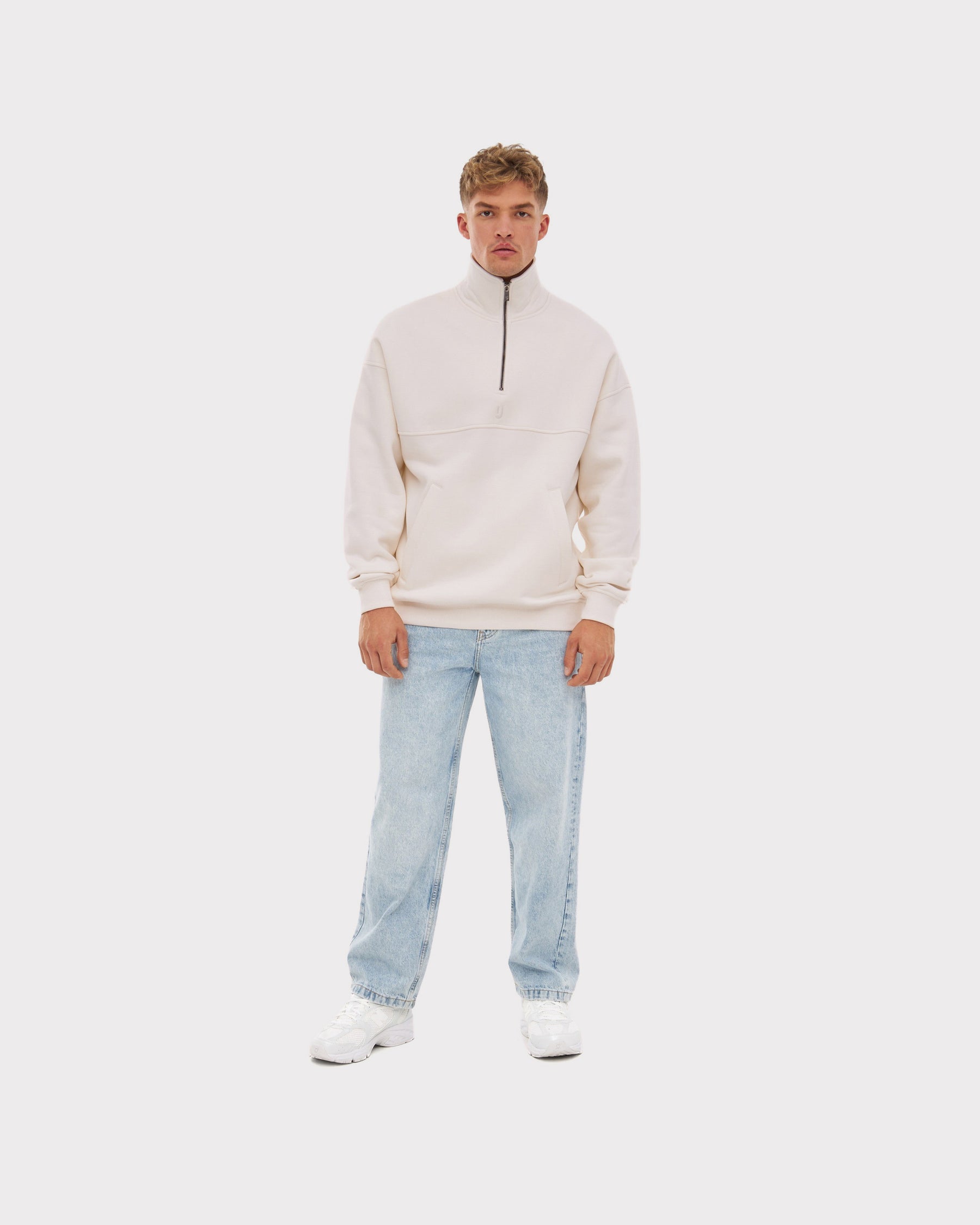 Herren trägt cremeweißen Half Zip Sweatshirt 'Cooper' mit Reißverschluss bis zur Brust und hellblaue Jeans