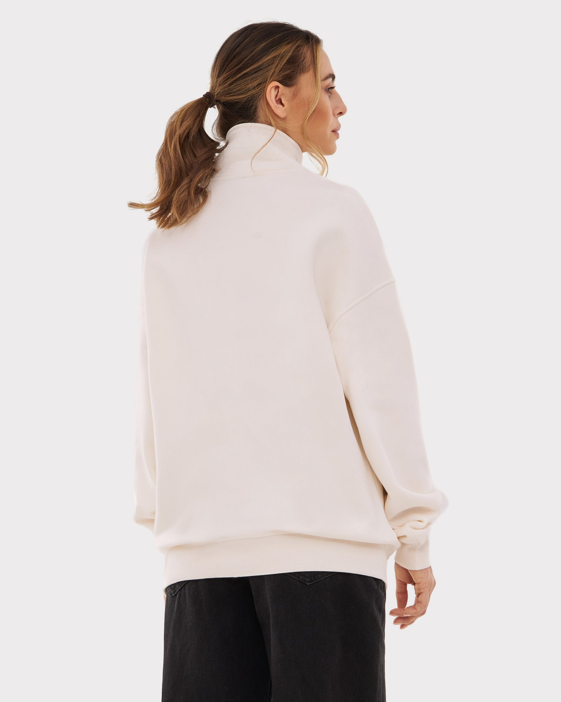 Frau von hinten in cremeweißem Half-Zip-Sweatshirt ‚Cooper‘ mit hohem Kragen und schwarzen Hosen