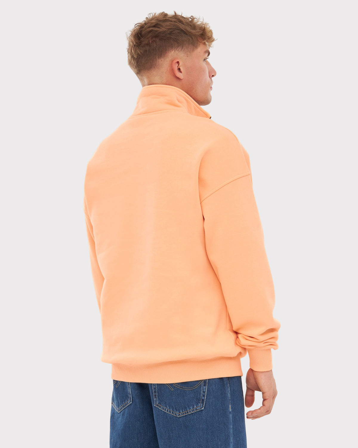 Mann trägt hellorangefarbenen Half Zip Sweatshirt 'Cooper', Rückansicht, blaue Jeans