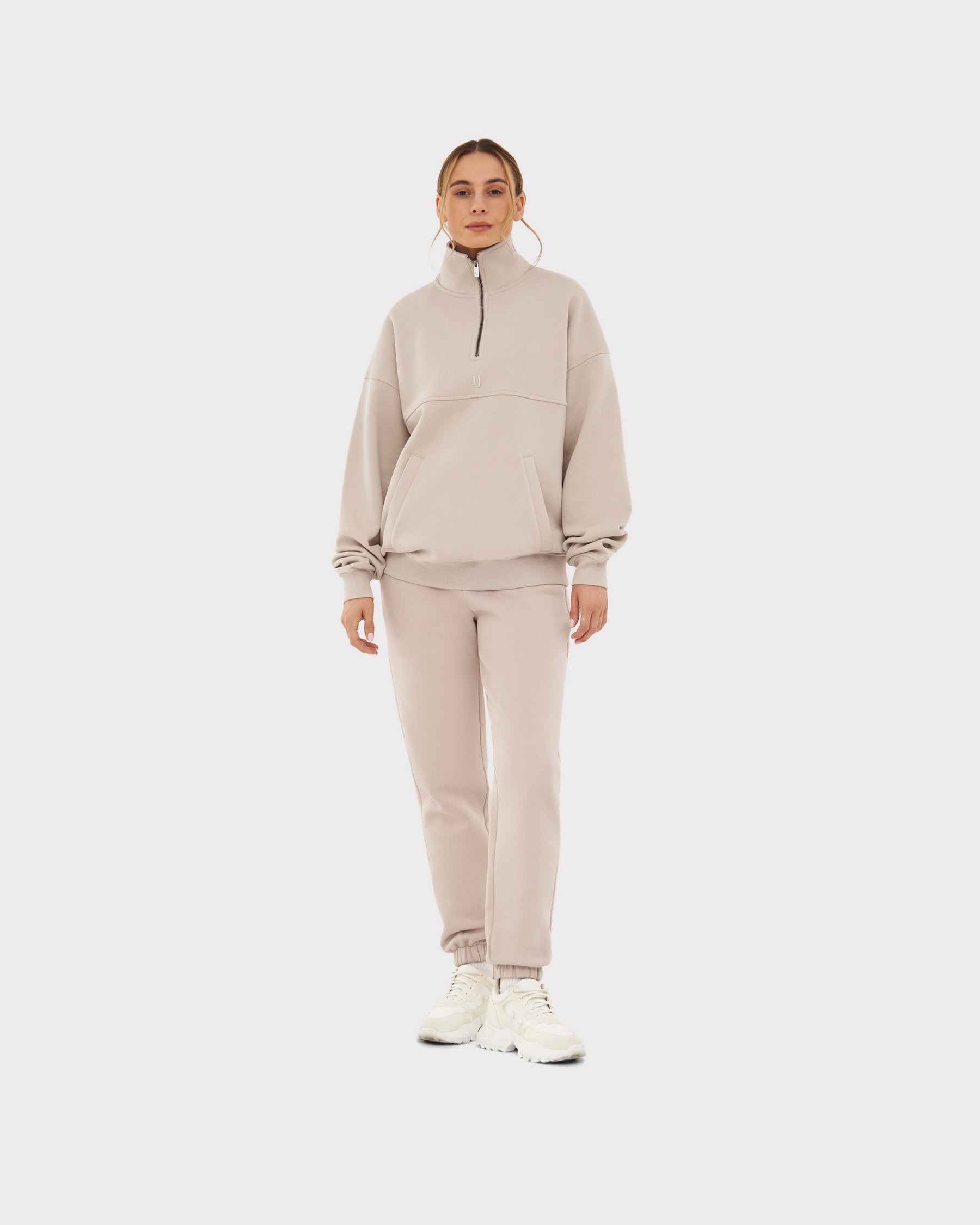 Frau trägt beigen Half-Zip-Sweatshirt 'Cooper' und passende Jogginghose mit weißen Sneakers