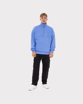 Mann trägt hellblauen Half-Zip Sweatshirt 'Cooper' mit hohem Kragen und Reißverschluss, schwarze Cargohose, weiße Turnschuhe