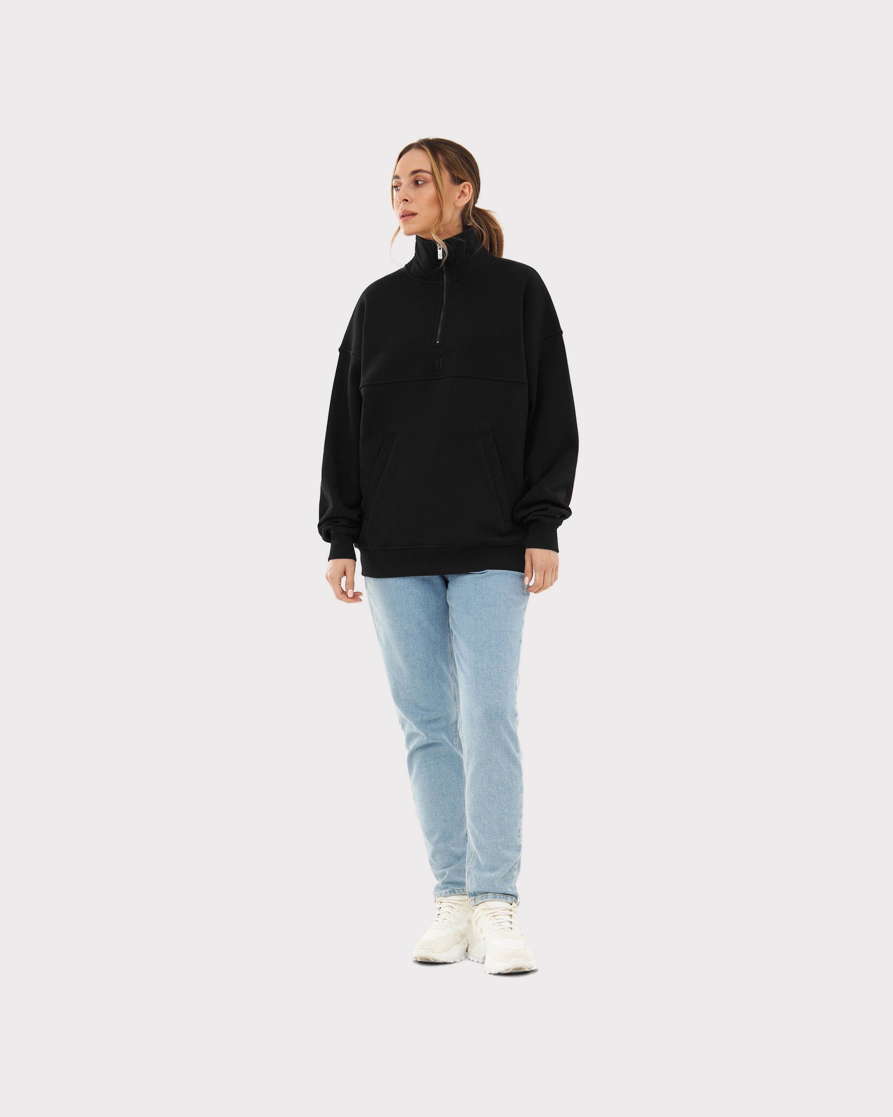 Frau trägt schwarzen Half Zip Sweatshirt 'Cooper' mit Stehkragen, kombiniert mit hellblauen Jeans und weißen Schuhen