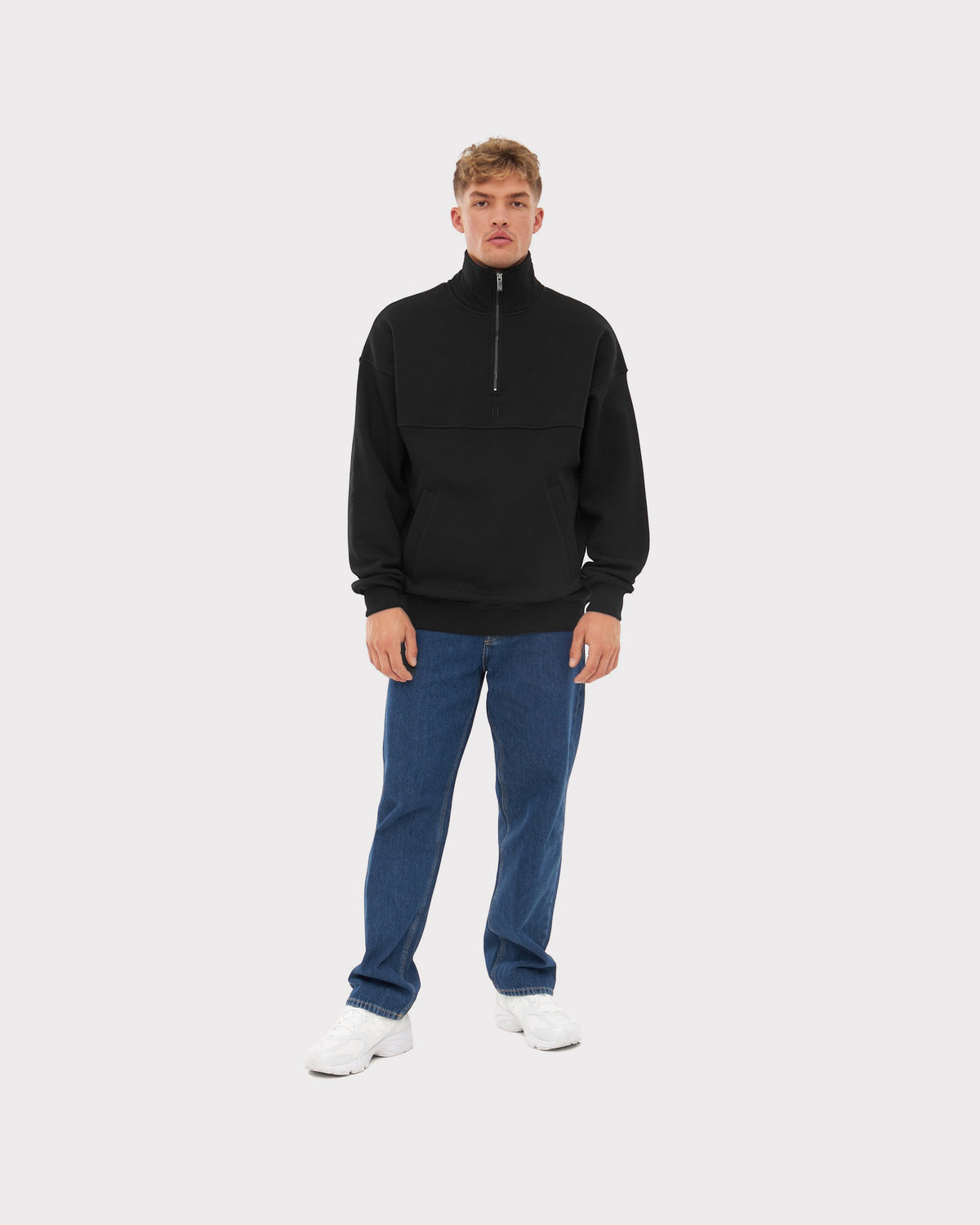 Mann trägt schwarzen Half Zip Sweatshirt Pullover 'Cooper', blaue Jeans und weiße Sneaker