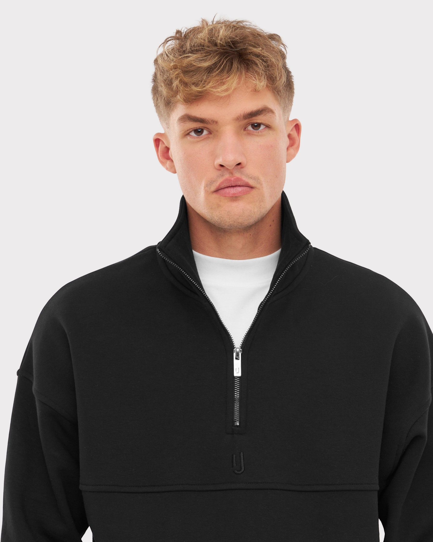 Mann trägt schwarzen Half Zip Sweatshirt 'Cooper' mit halb offenem Reißverschluss und weißem Unterhemd