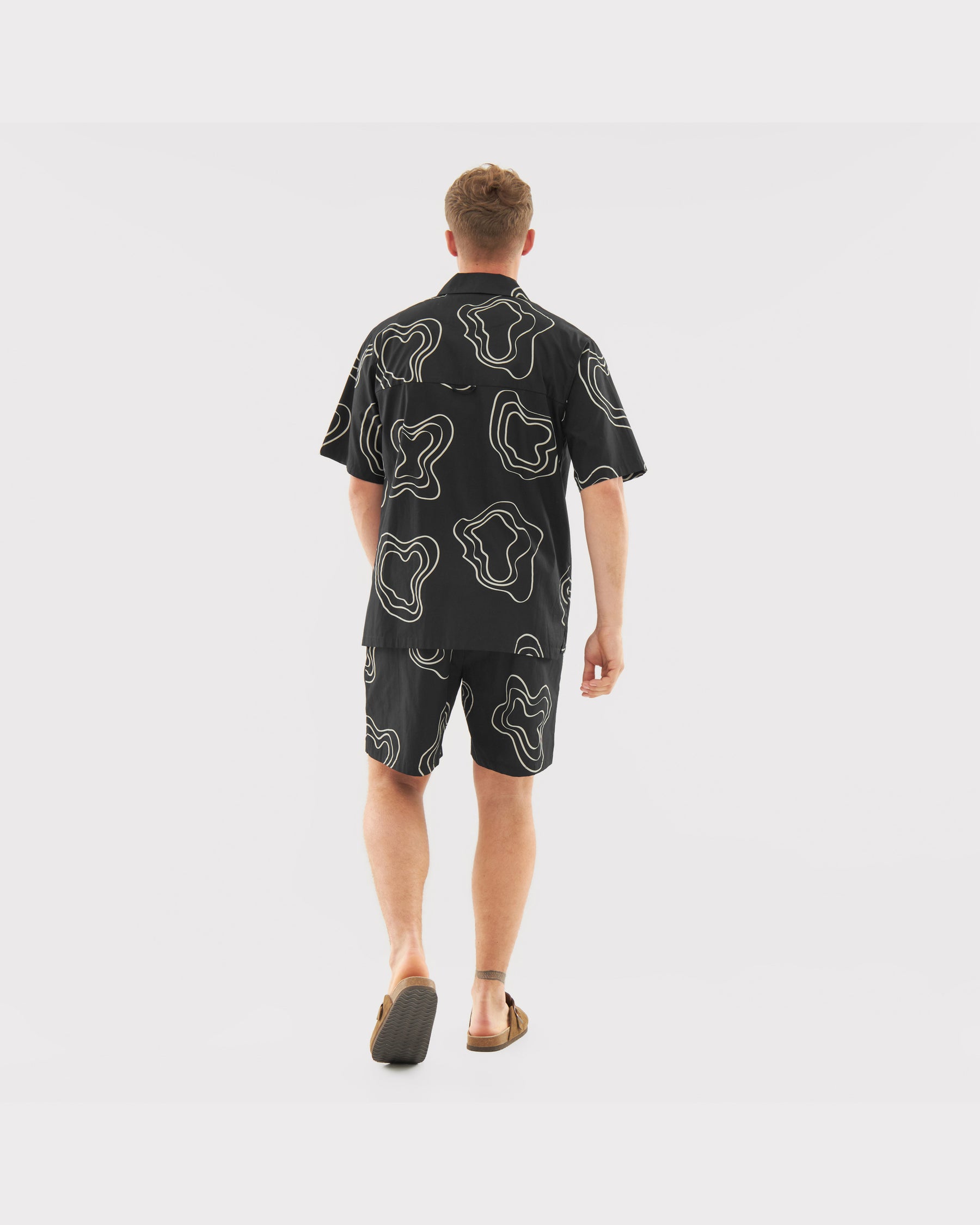 Mann von hinten mit schwarzem Hemd und Shorts mit weißem, abstraktem Muster aus Set 'Spencer'