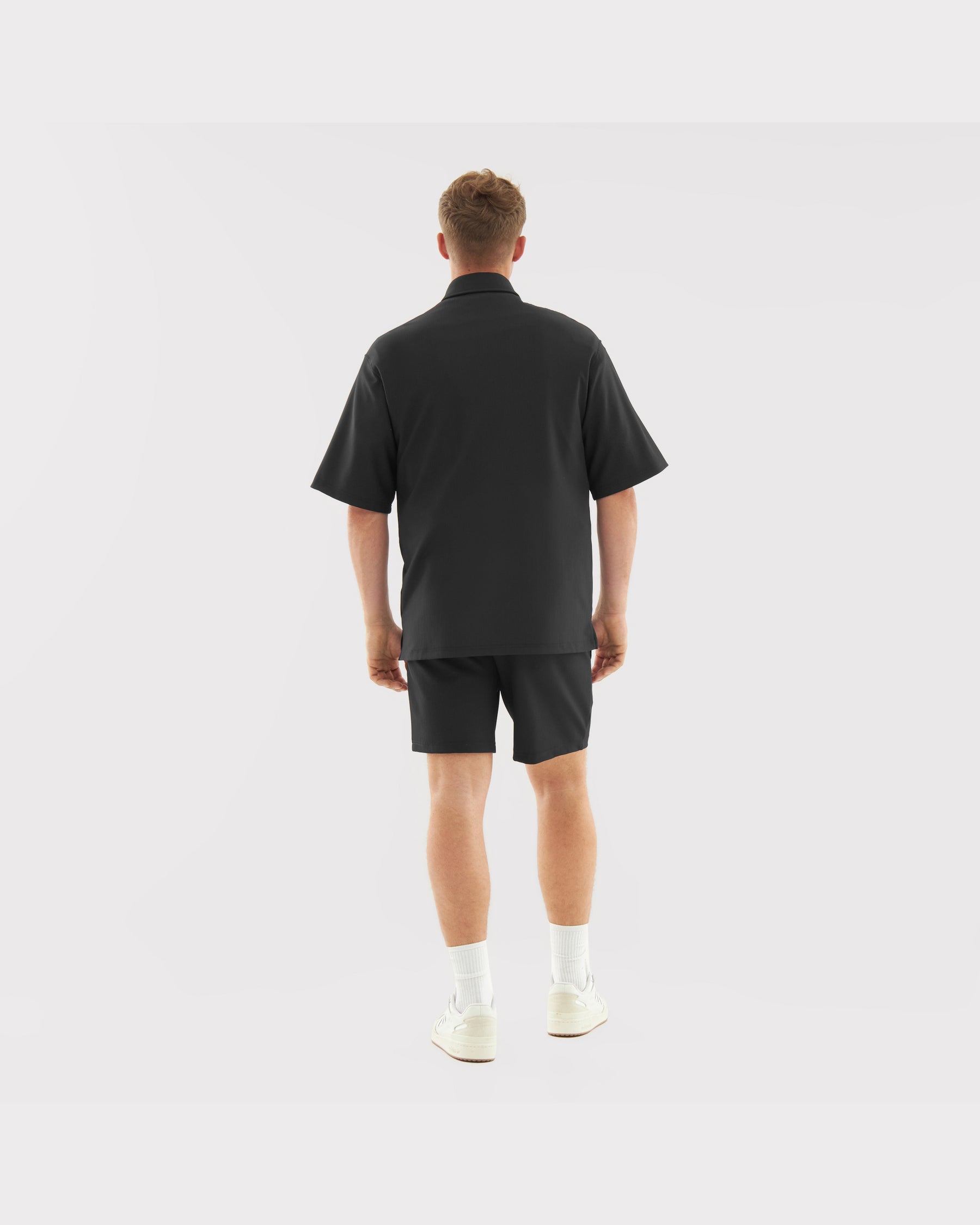 Mann von hinten in lockerem, schwarzem Oversize-Hemd und passenden Shorts aus dem Set 'Mason'