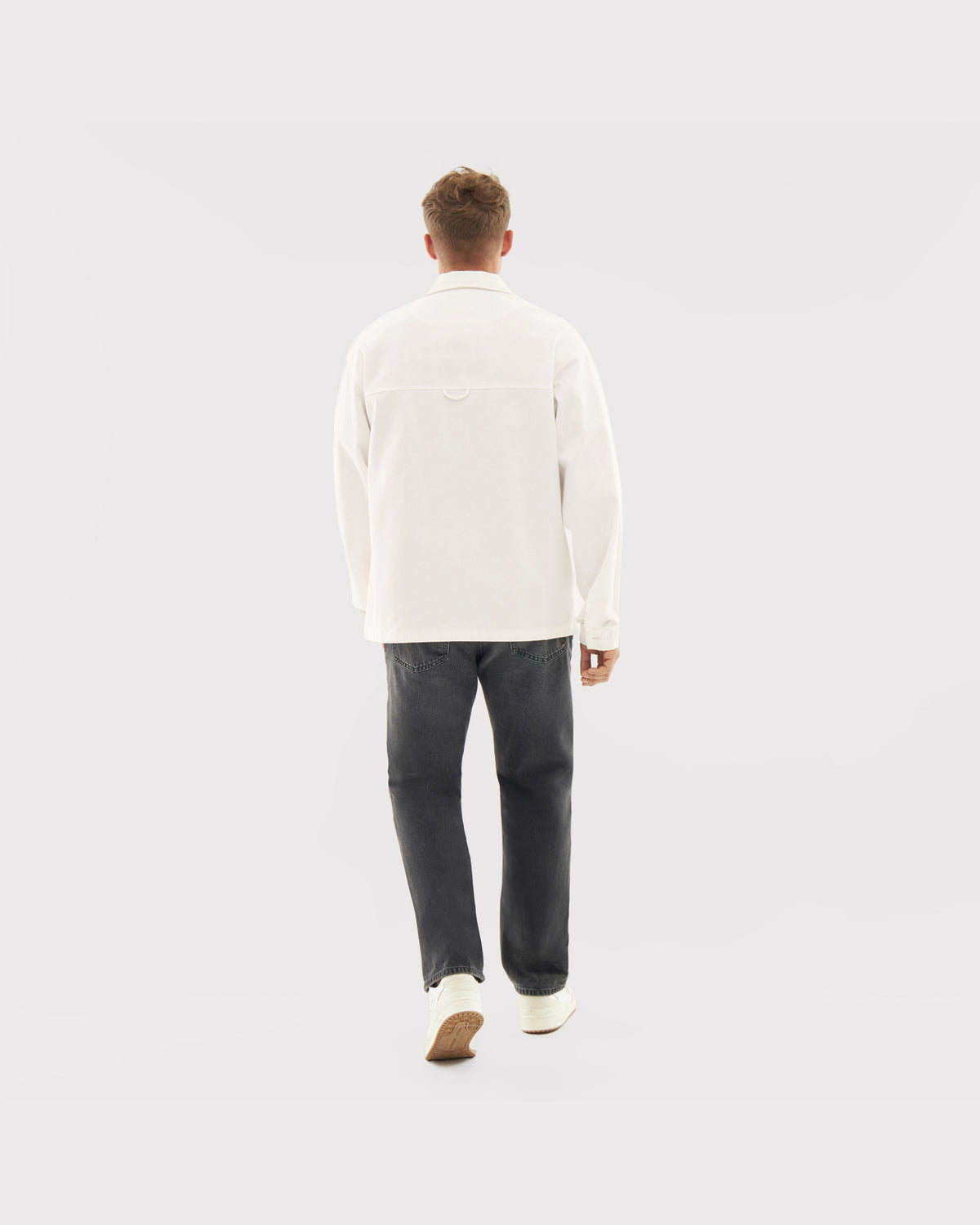 Rückansicht eines Mannes mit weißem Overshirt 'Cameron', dunkler Jeans und weißen Schuhen