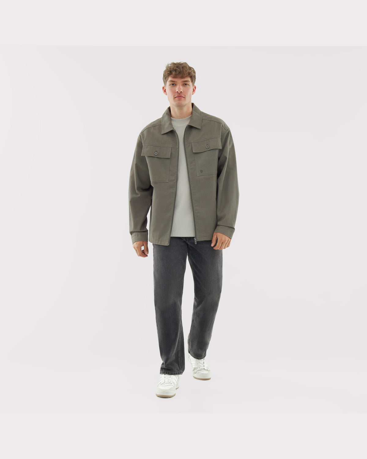 Mann trägt olivgrüne Overshirt 'Cameron' aus Baumwolle mit zwei Brusttaschen, kombiniert mit weißem T-Shirt, schwarzen Jeans und weißen Sneakern