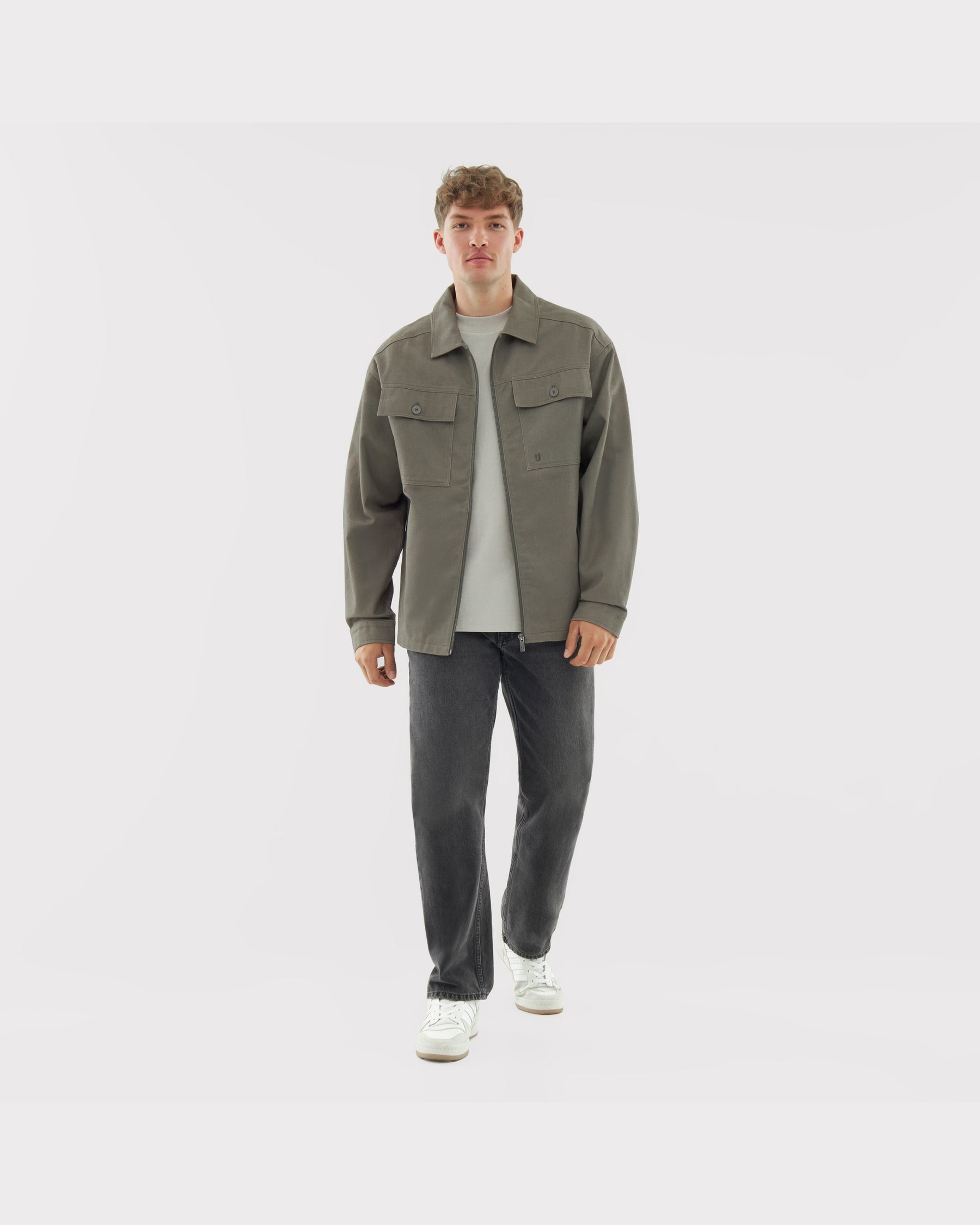 Mann trägt olivgrüne Overshirt 'Cameron' aus Baumwolle mit zwei Brusttaschen, kombiniert mit weißem T-Shirt, schwarzen Jeans und weißen Sneakern