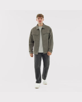 Mann trägt olivgrüne Overshirt 'Cameron' aus Baumwolle mit zwei Brusttaschen, kombiniert mit weißem T-Shirt, schwarzen Jeans und weißen Sneakern