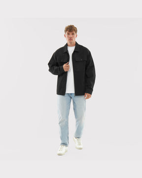 Mann trägt schwarze Baumwoll-Overshirt 'Cameron', weiße T-Shirt, helle Jeans und weiße Sneaker