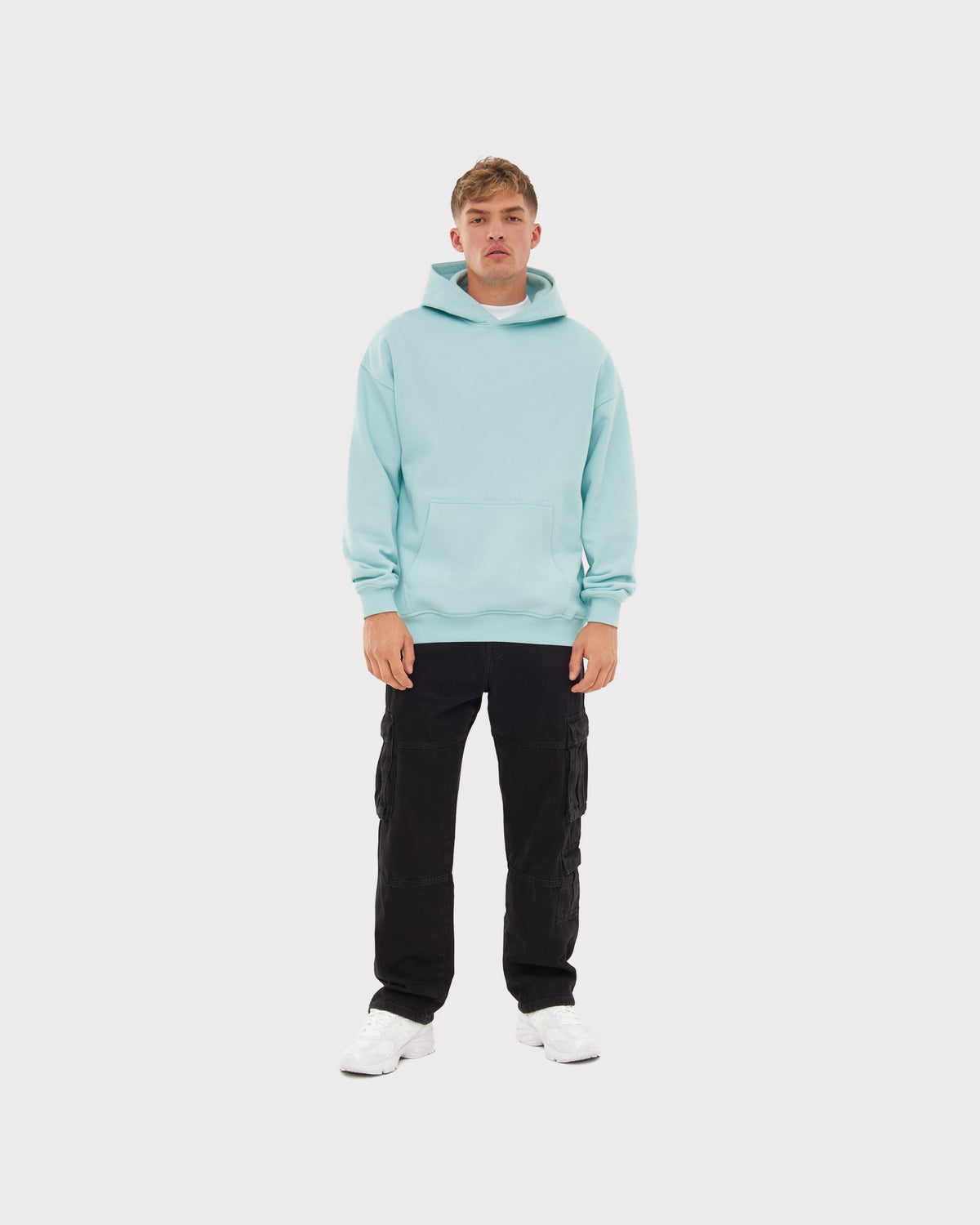 Mann trägt oversized Hoodie 'Cody' in eisblau mit schwarzer Cargo-Hose und weißen Sneakern