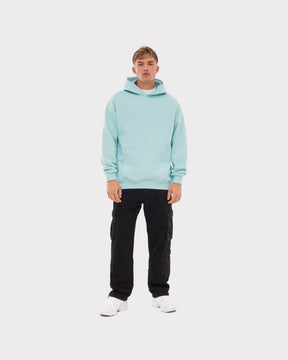 Mann trägt oversized Hoodie 'Cody' in eisblau mit schwarzer Cargo-Hose und weißen Sneakern