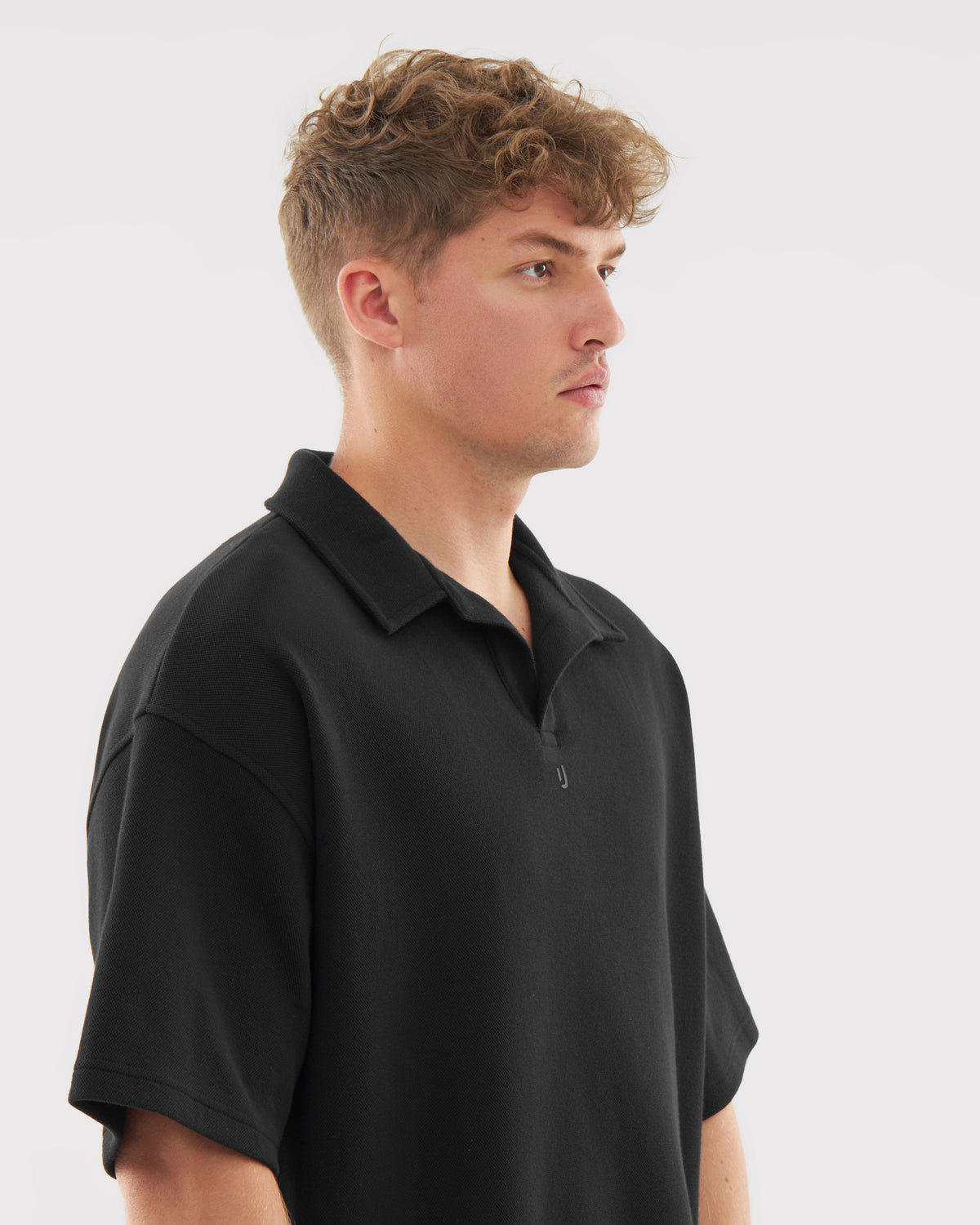 Mann trägt schwarzes Herren-Poloshirt mit kurzem Arm und offenem Kragen, seitliche Ansicht