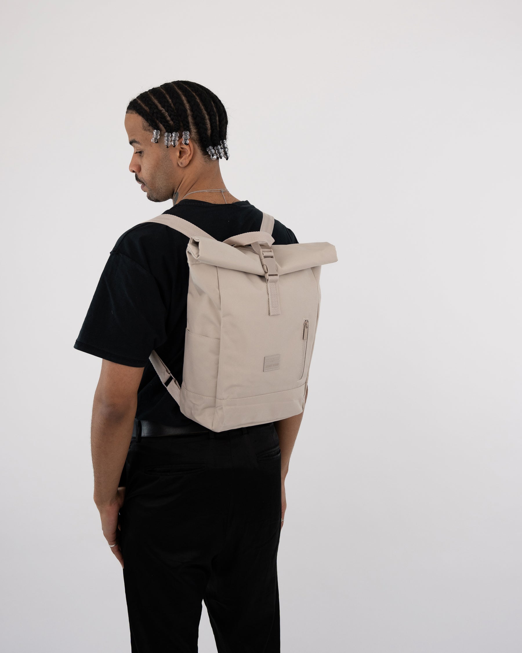 Mann trägt beigen Rolltop Rucksack 'Robin Small' von Johnny Urban, schwarze Kleidung