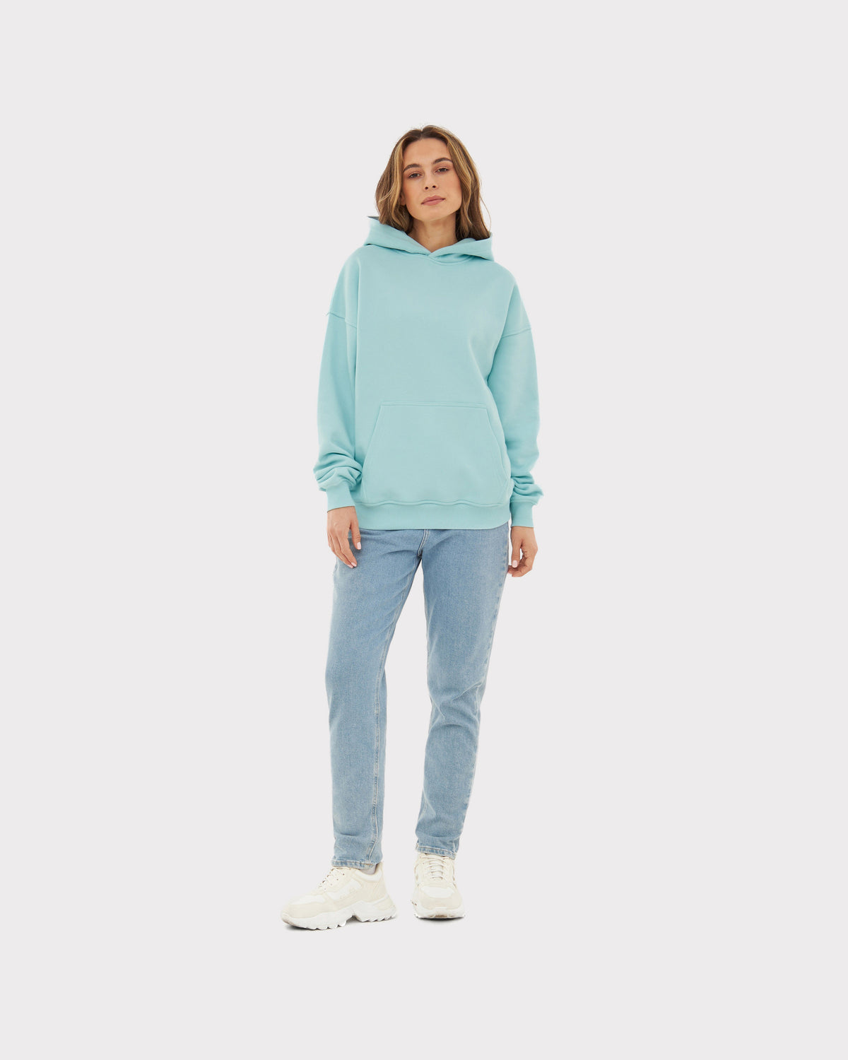 Frau trägt oversized Hoodie 'Cody' in eisblau mit großer Tasche vorne, dazu helle Jeans und weiße Sneaker