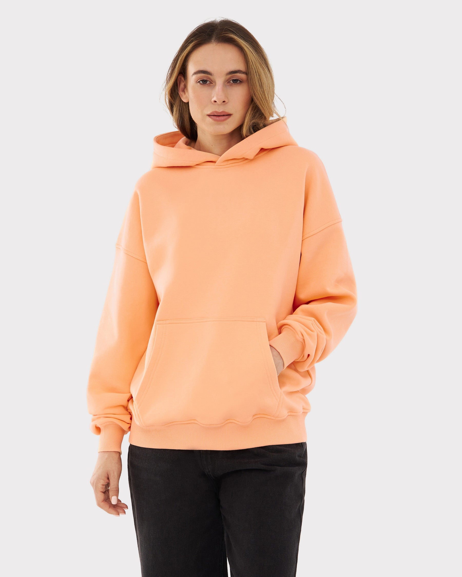 Frau trägt oversized Hoodie 'Cody' in Pfirsichfarben mit Kängurutasche und Kapuze