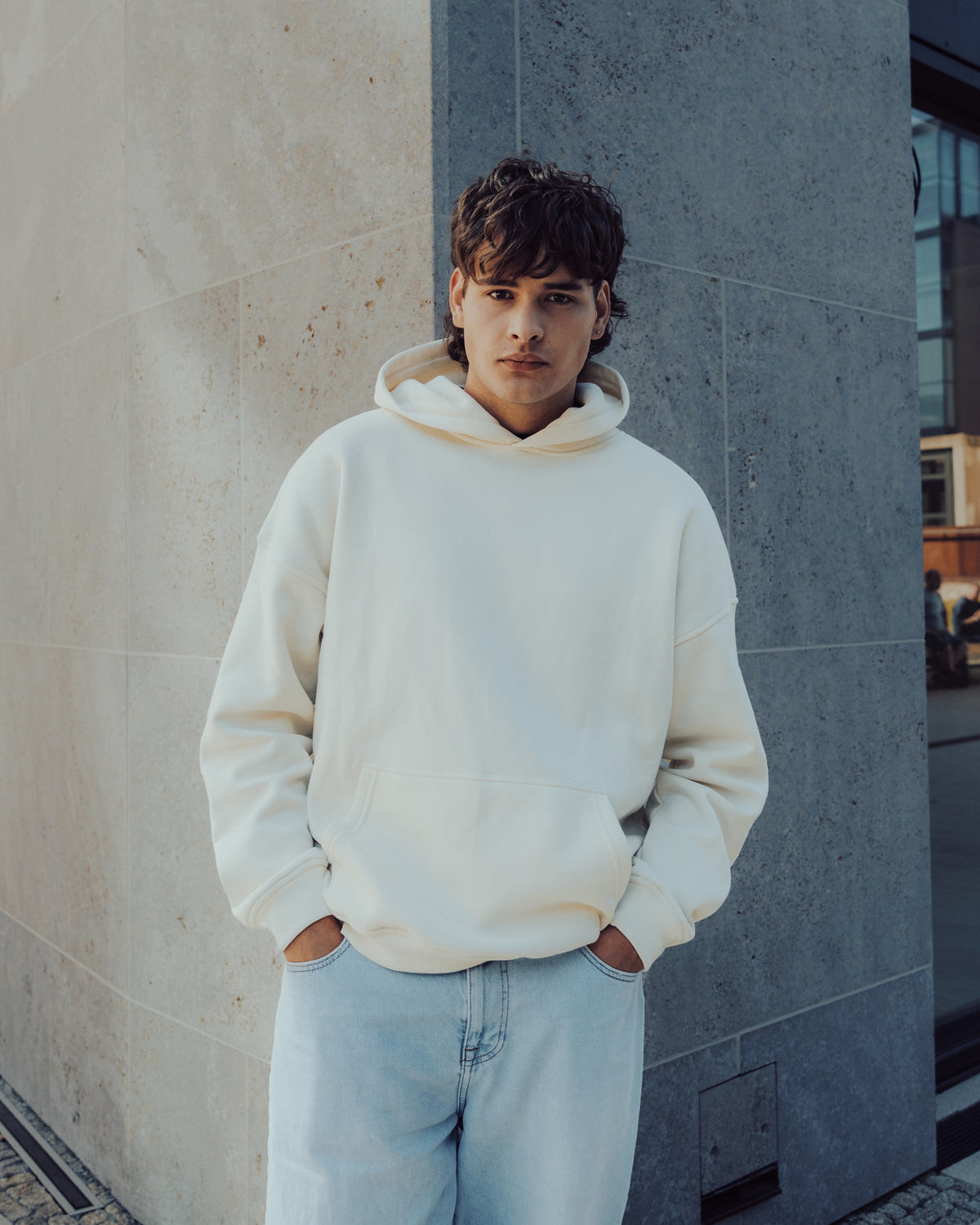 Mann trägt oversized Hoodie 'Cody' von Johnny Urban in weiß vor modernem Gebäude