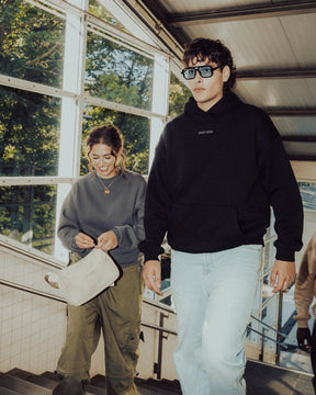 Junger Mann trägt schwarzen oversized Hoodie 'Cody' mit 'Johnny Urban' Print und helle Jeans, begleitet von zwei Personen auf Treppe
