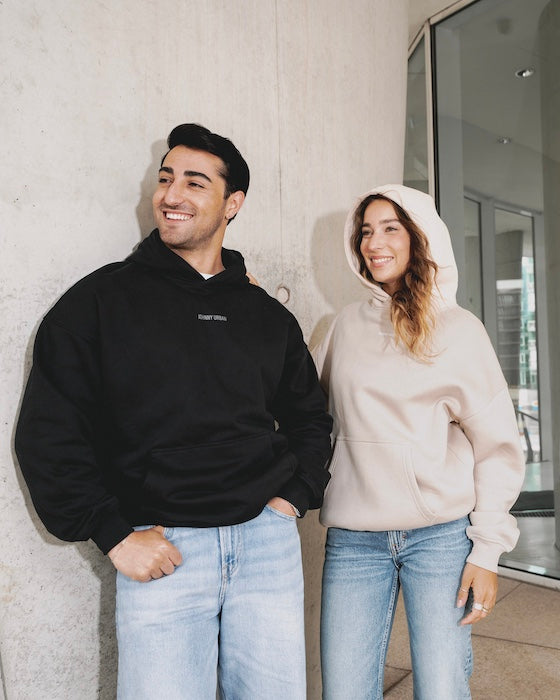 Mann und Frau vor einer Betonwand in Johnny-Urban-Pullovern in Schwarz und Beige. 