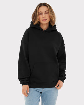 Frau trägt oversized Hoodie 'Cody' in Schwarz mit Kapuze und Kängurutasche, kombiniert mit blauen Jeans