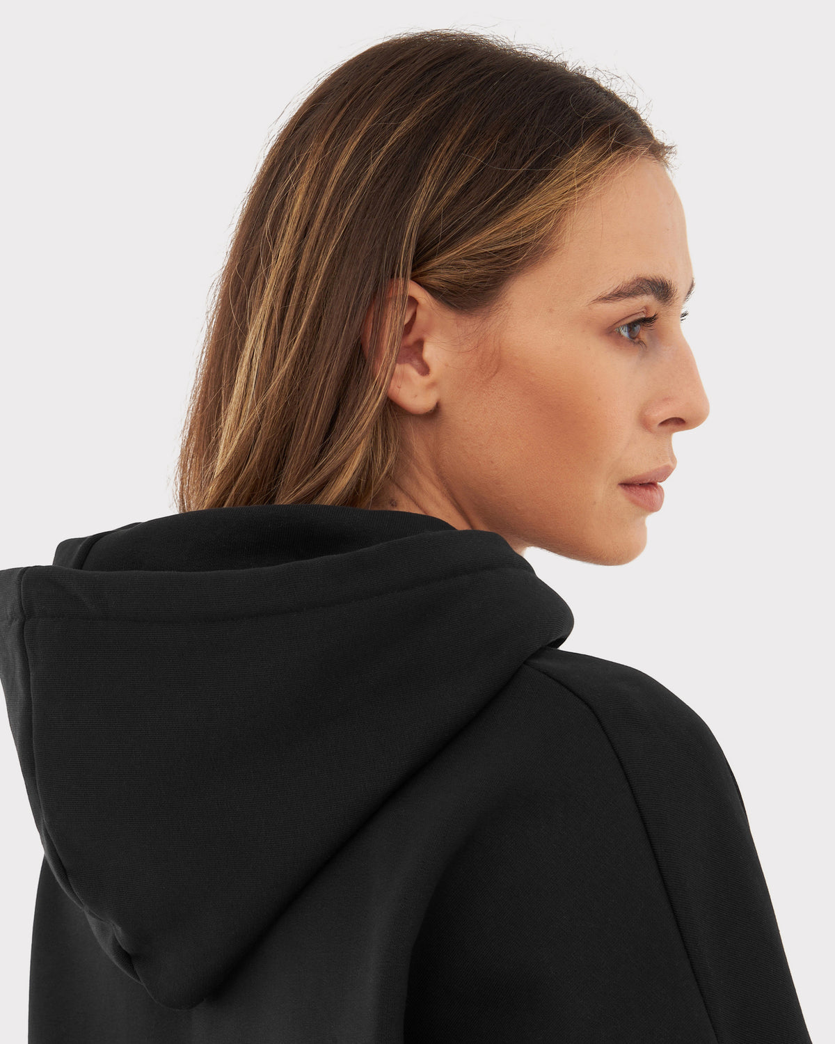 Frau mit mittelbraunen Haaren trägt Oversized Hoodie 'Cody' in Schwarz, Blick nach rechts