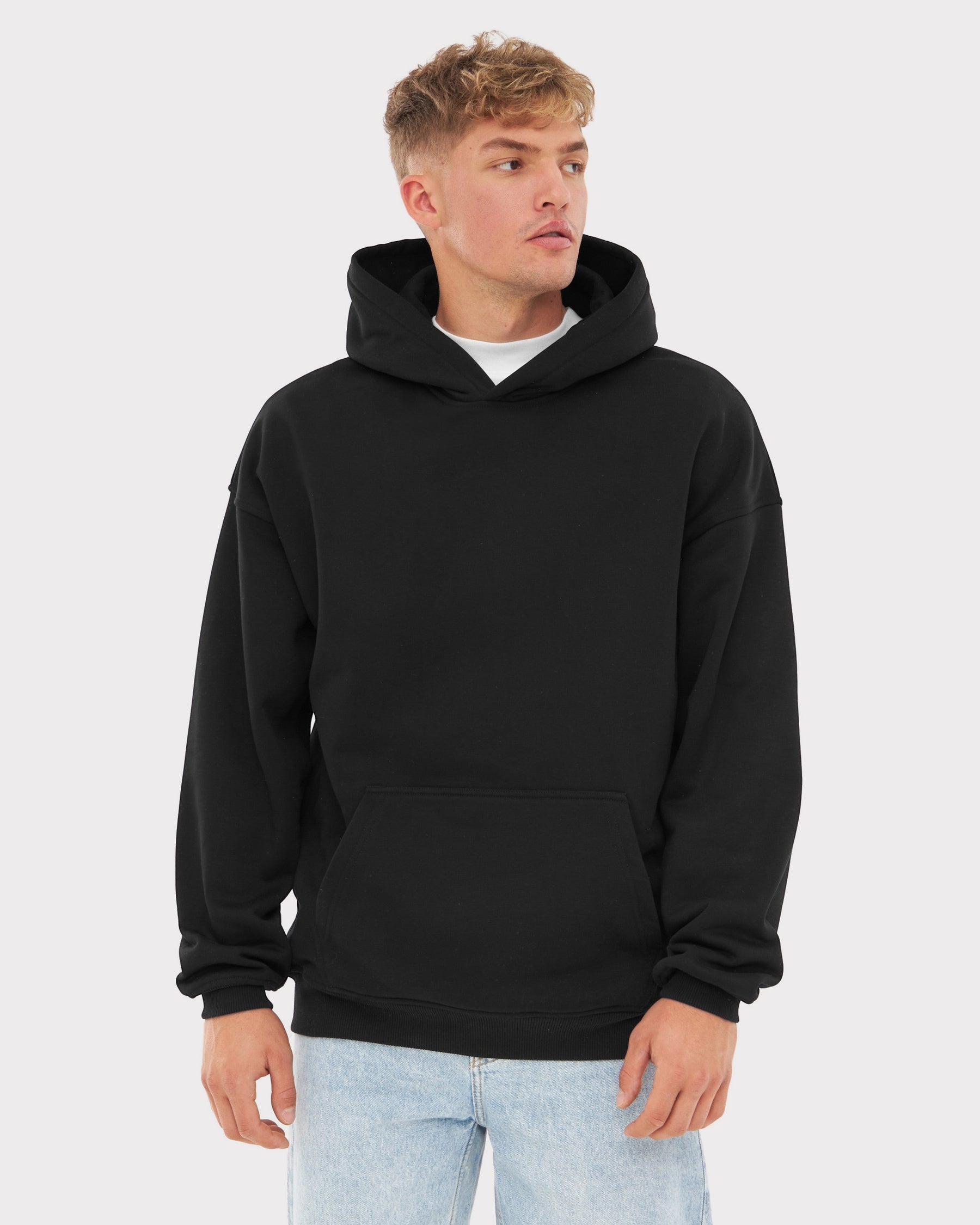 Mann trägt schwarzen oversized Hoodie 'Cody' mit Kängurutasche und Kapuze, kombiniert mit hellblauen Jeans
