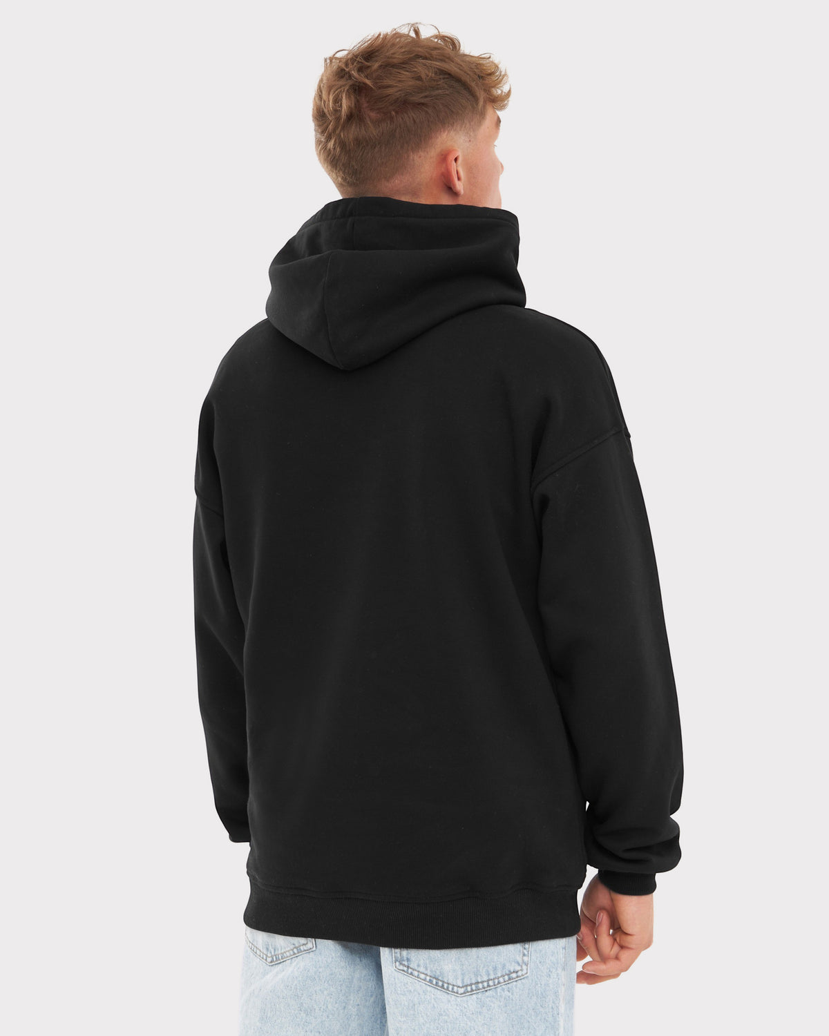 Mann trägt schwarzen Oversized Hoodie 'Cody' von hinten, dazu helle Jeans