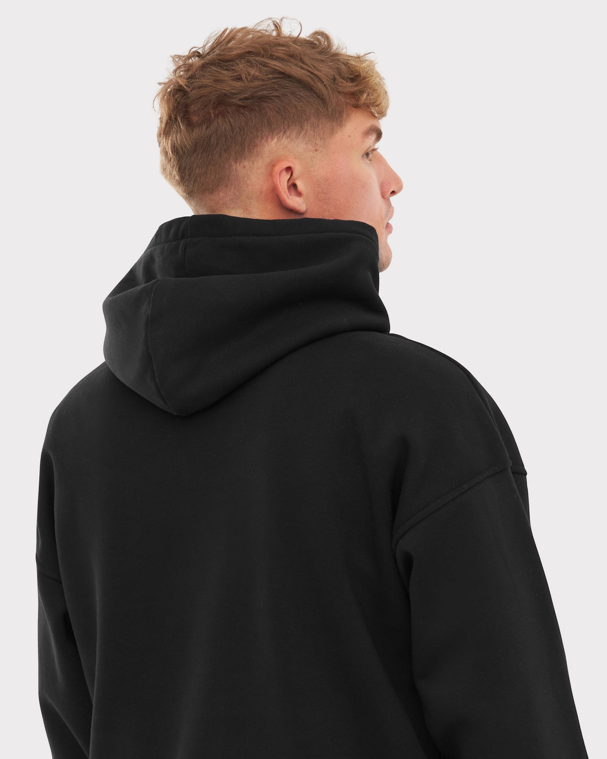 Rückansicht eines Mannes mit kurzem, blondem Haar, der einen schwarzen, oversized Hoodie namens 'Cody' trägt