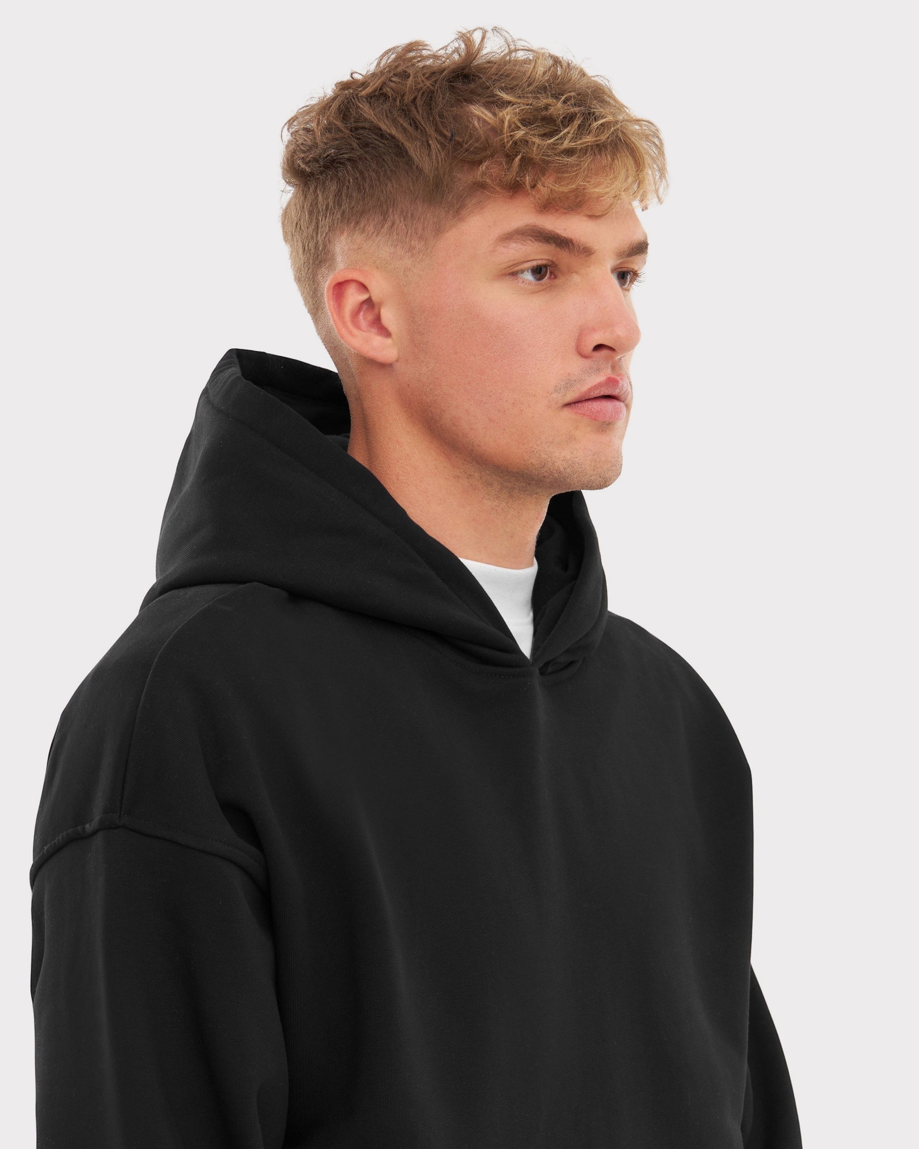 Mann mit kurz blondem Haar trägt schwarzen Oversized Hoodie 'Cody' von Johnny Urban