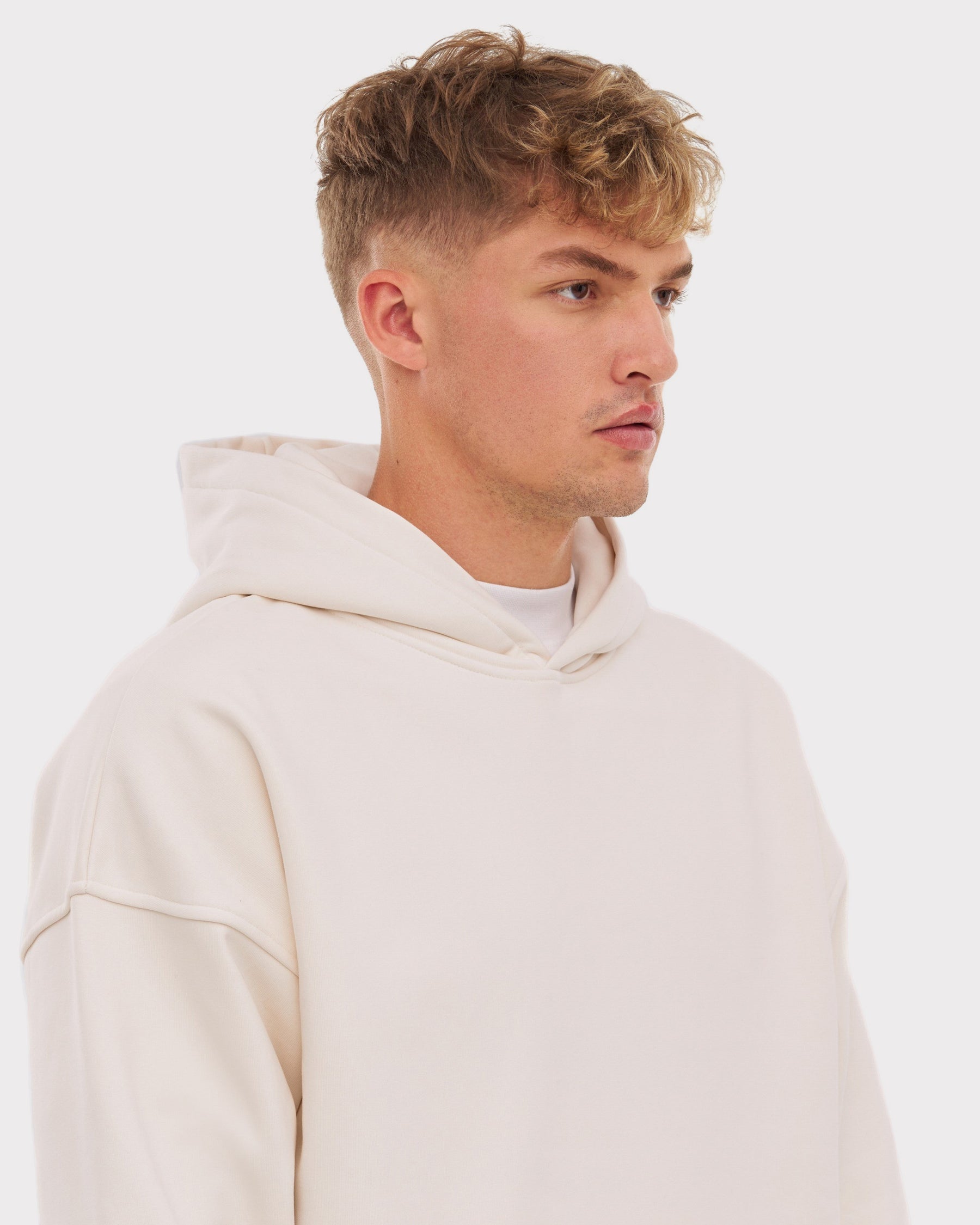 junger Mann mit kurzem lockigem Haar trägt weißen oversized Hoodie 'Cody'