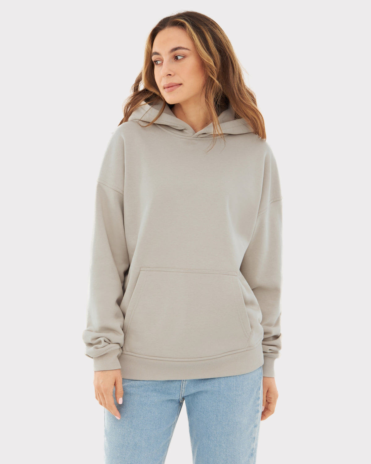 Frau trägt beigen Oversized Hoodie 'Cody' mit Kapuze und Kängurutasche, kombiniert mit blauen Jeans