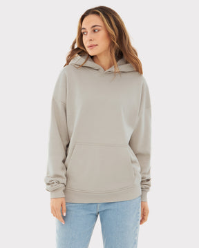 Frau trägt beigen Oversized Hoodie 'Cody' mit Kapuze und Kängurutasche, kombiniert mit blauen Jeans